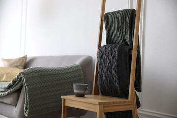 Knitted plaids on chair near sofa in living room