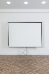 Blank projection screen near white wall indoors. Space for design