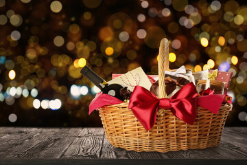 Wicker basket full of gifts on wooden table against blurred festive lights. Space for text