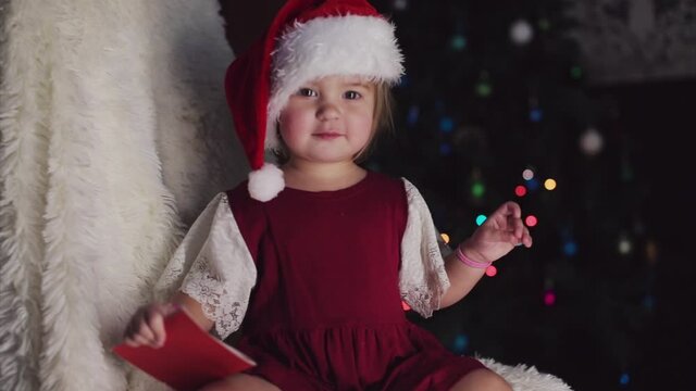 a child in red clothes is sitting waiting for the new year. the concept of celebrating Christmas at midnight. holiday costume. a girl writes a letter to Santa Claus. wish list
