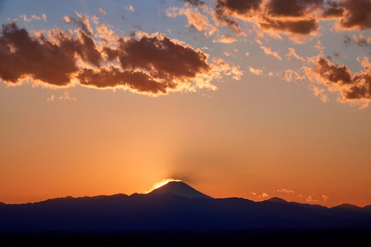 The peak of mountain Fuji with golden clouds and warm sunset light, summer time, Kofu, Yamanashi, Japan. The mountain range in front shows the how big of Mt. Fuji is.