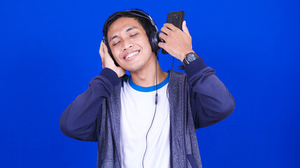 Naklejka premium asian man listening music with happy expression wear handphone and headphone isolated blue background