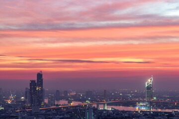 Fototapeta na wymiar Bangkok, thailand - Dec 23, 2020 : Aerial view of Bangkok city Overlooking Skyscrapers and the Bridge crosses the Chao Phraya river with bright glowing lights at dusk. No focus, specifically.