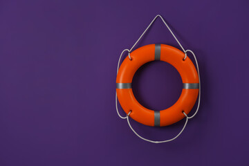 Orange lifebuoy and space for text on violet background. Rescue equipment