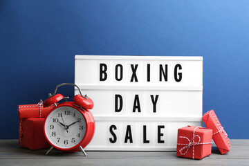 Composition with Boxing Day Sale sign and Christmas gifts on white table against blue background
