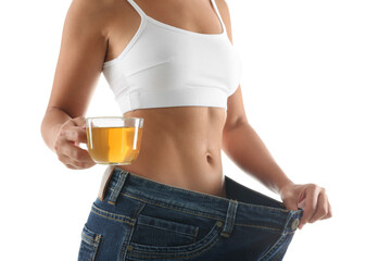 Young woman in old big jeans with cup of tea showing her diet results on white background, closeup