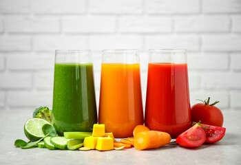 Different tasty juices and fresh ingredients on grey table against brick wall