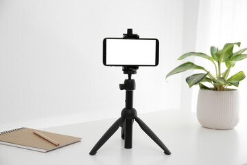 Smartphone with blank screen fixed to tripod on white table indoors. Mockup for design - obrazy, fototapety, plakaty