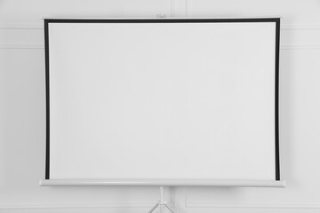 Obraz premium Blank projection screen near white wall indoors. Space for design
