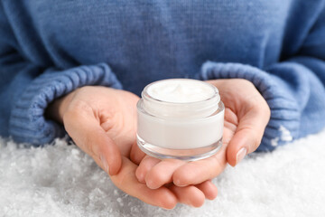 Woman holding jar of cream above decorative snow, closeup. Cosmetic product for winter
