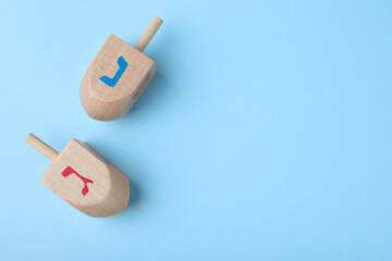 Hanukkah traditional dreidels with letters Nun and Gimel on light blue background, flat lay. Space for text