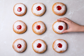 Woman taking Hanukkah doughnut with jelly and sugar powder at grey table, top view