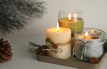 Composition with burning scented conifer candles and Christmas decor on light table