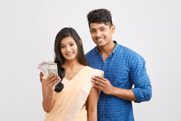 Exited cheerful young couple holding Indian currency on white