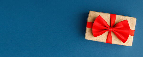 Gift in craft box with red bow on classic blue background. Surprise your loved one. The concept of the day of St. Valentine's, weddings, birthday, New Year, Christmas, dad or mom day