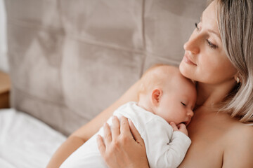 mom is mom is lying down with a baby in a white bed after feeding breast milk. 