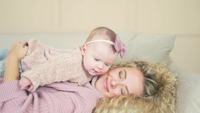 Happy Carefree Mother, Cute Small Child Daughter Laughing Having Fun Lying on Sofa and Playing, Smiling Mum Enjoying Bonding Lifting Baby Cuddling Hugging Spending Time with Little Funny Kid at Home