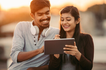 Happy young friends using tablet with headphones at outdoor.
