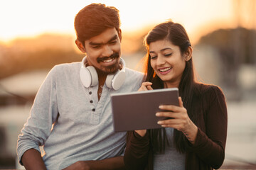 Happy young friends using tablet with headphones at outdoor.