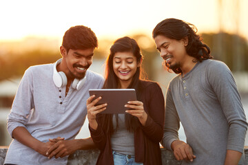 Cheerful young friends playing in digital tablet on terrace at outdoor.