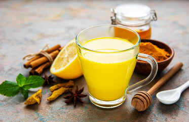 Yellow turmeric latte drink. Golden milk with cinnamon, turmeric, ginger  and honey over concrete background.