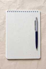  Gray notepad with white coiled spring and pen on a background of beige crumpled craft paper