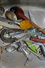 Dirty spoons, forks and a knifes in the sink. Washing dirty dishes.