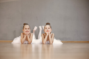 Cute little ballerinas in white ballet costume. Children in a pointe shoes is dancing in the room. Kid in dance class.