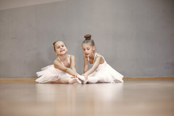Cute little ballerinas in white ballet costume. Children in a pointe shoes is dancing in the room....
