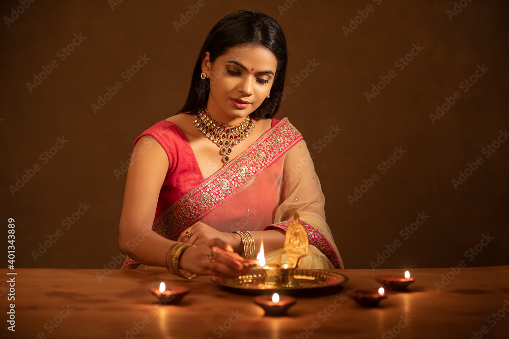 Wall mural Beautiful Hindu Indian young women lightening Diya on Diwali day.