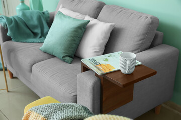 Cup of tea and magazine on armrest table in room