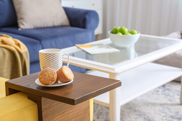 Cup of tea and cupcakes on armrest table in room