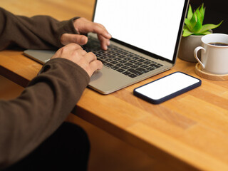 Male hands typing on laptop keyboard on wooden table with smartphone