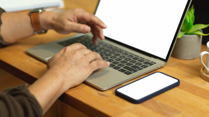 Male hands typing on laptop keyboard on wooden table with smartphone