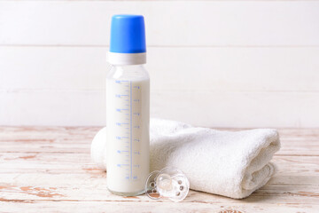 Fototapeta na wymiar Bottle of milk for baby with pacifier and towel on wooden background