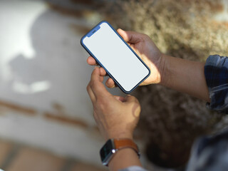 Cropped shot of male hands using smartphone while relaxing in garden