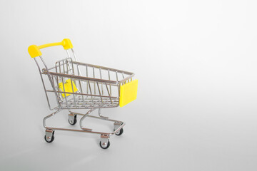 Grocery cart with yellow handle on a gray background. Side view. Horizontal format. Copyspace