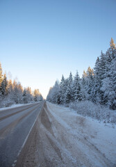 Car paved road in the middle of a snow-covered forest under a bright blue sky.