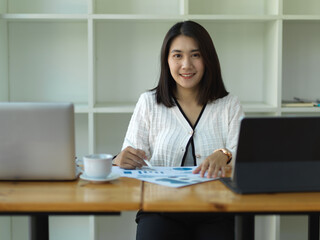Businesswoman smiling to camera while reading paperwork in office room