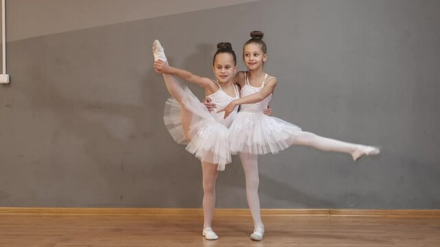 Two flexible little ballerinas are standing in the vertical splits in a ballet class.