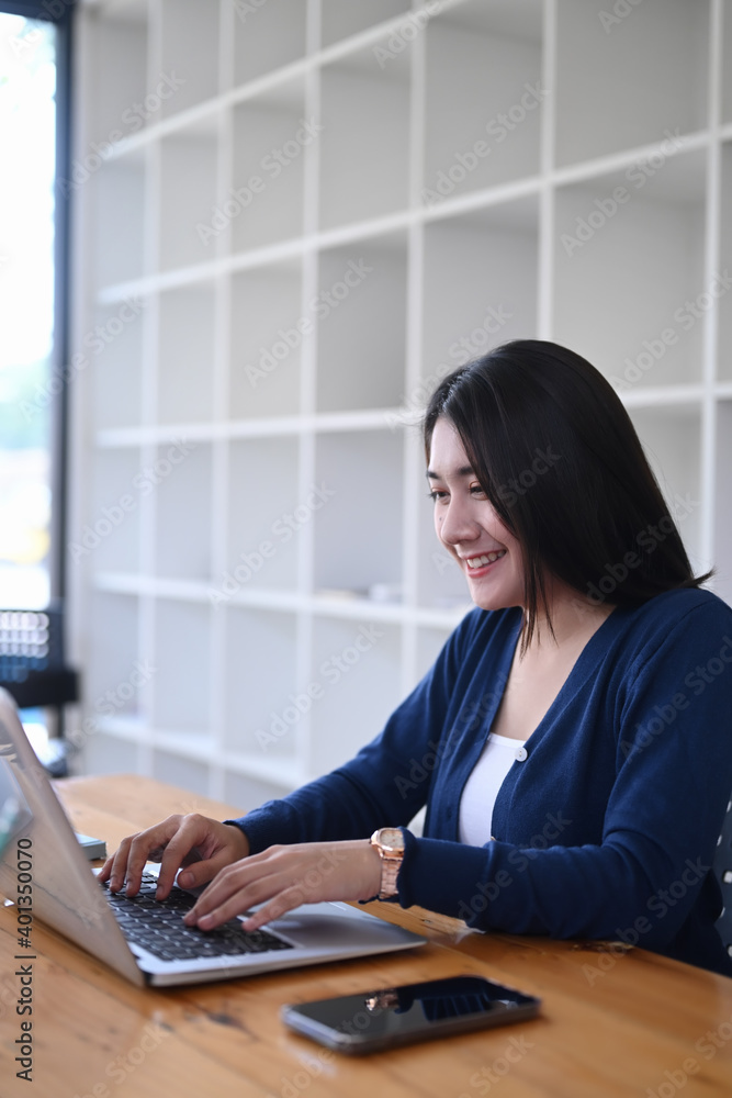 Poster side view of female college student doing assignments with laptop computer and sitting at the librar