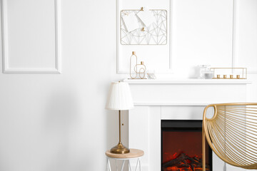 Fireplace with armchair, table and lamp in stylish interior of room