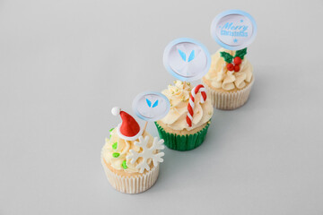 Tasty Christmas cupcakes on light background