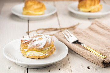 Profiterole cake on white wooden table. Creamy filling and crunchy dough on the bottom and top of the cake. In Slovakia traditional wedding cake. Served with golden fork in natural warm colors.