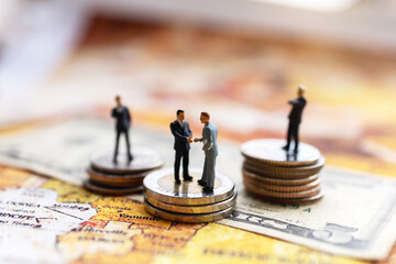 Miniature people: Businessman handshake with coins stack on world map,  Investment, agreement, partnership and business concept