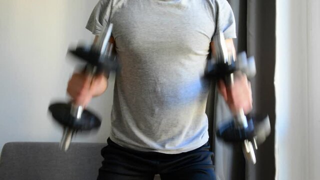 A young man is working out at home by doing exercise for brachialis with dumbbells