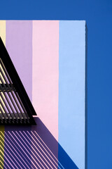 Sunlight and shadow of awning on surface of pastel building wall against blue sky in vertical frame, Abstract architecture background and building exterior concept