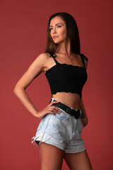 beautiful woman in a black top and denim shorts posing in the studio on a red background