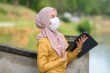 Asian muslim student woman with traditional dress wearing medical face mask at le lake