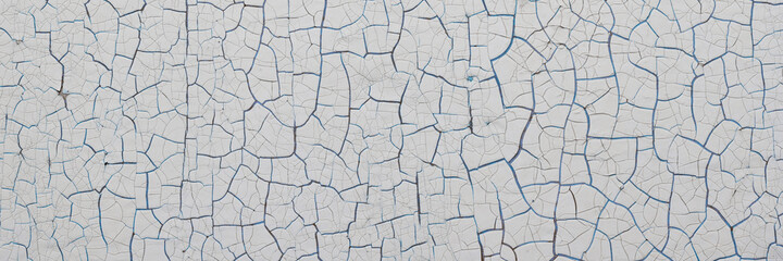 Peeling paint on the wall. Panorama of a concrete wall with old cracked flaking paint. Weathered rough painted surface with patterns of cracks and peeling. Panoramic texture for background and design.